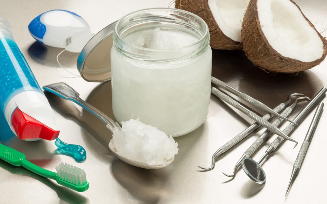 Jar of coconut oil next to spoonful of coconut oil, toothbrush, toothpaste, coconuts, and dental equipment.