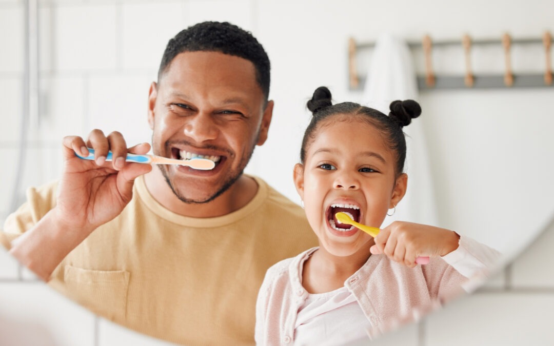 Happy father and daughter brushing their teeth in the mirror.