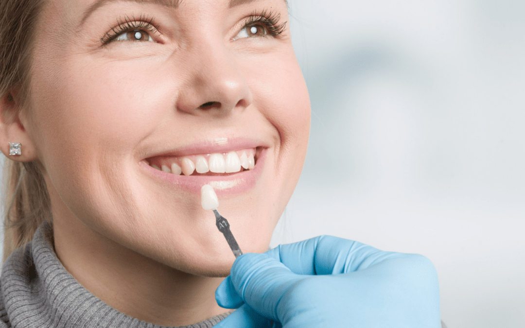 Woman smiling as dentist holds up sample tooth next to her teeth.